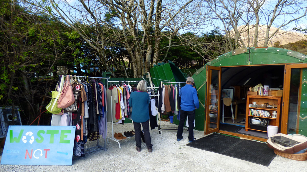 two people look at items in a shed and clothes rail outdoors
