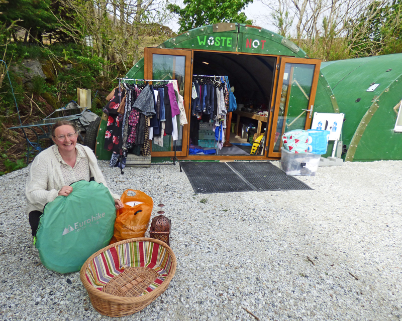 woman with a basket and other items infront of a green stall