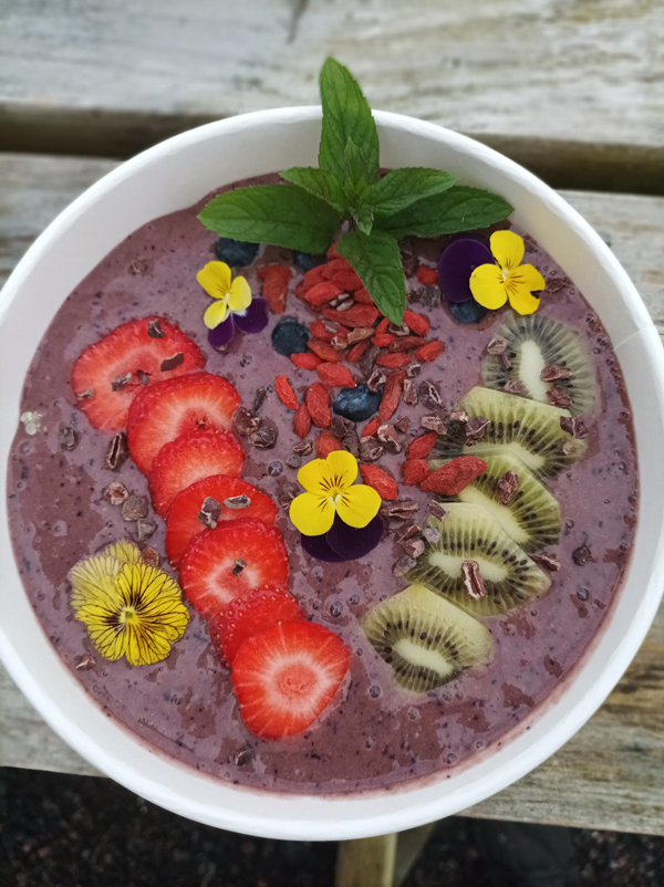 while bowl with purple contents decorated with flowers and sliced vegetables