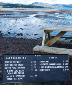 menu board leaning on picnic table with bay and mountains in background