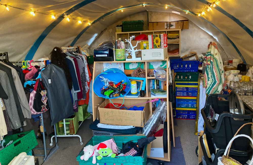 shelves with books and bric a brac , racks of clothing inside semicircular tent with fairy lights