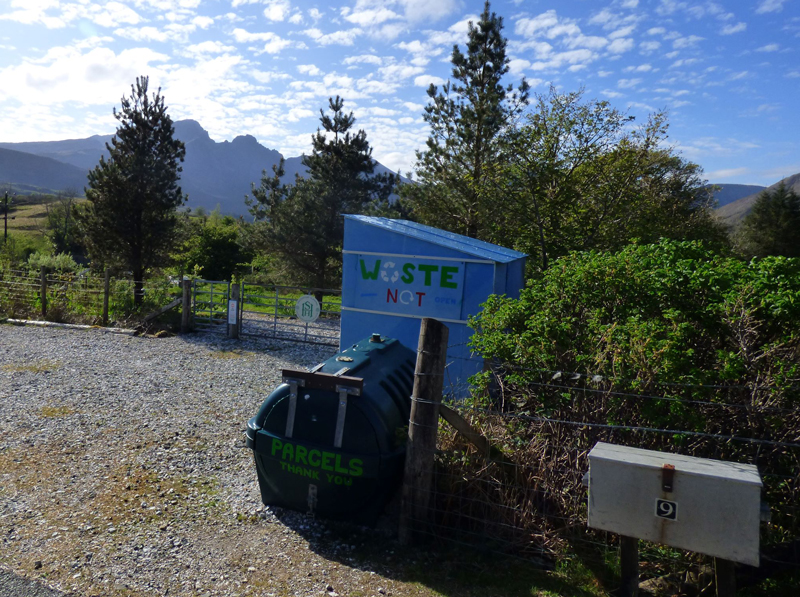blue metal bin on gravel in front of trees and hills
