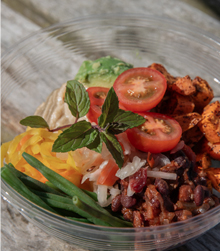 wooden table with glass dish containing tomatoes, green beans, rice and beans with sprig of mint